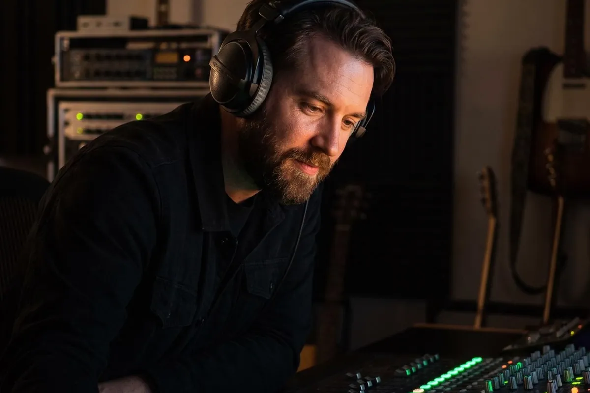 A music producer with headphones at a mixing desk in a dark studio